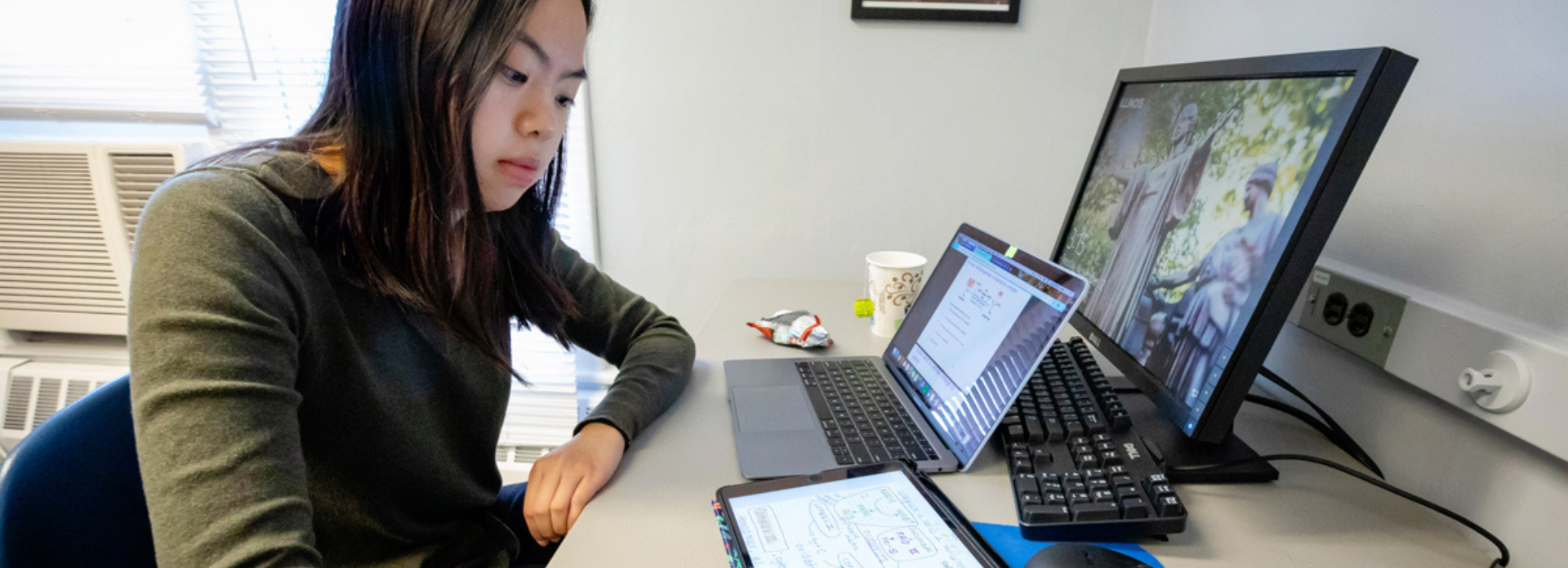 student sits and works at her desk with multiple computer screens