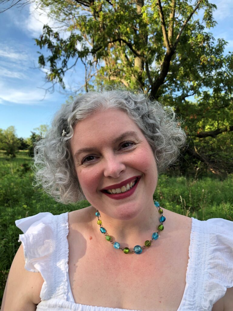 Cindy McKendall smiles at the camera while surrounded by nature and a blue sky