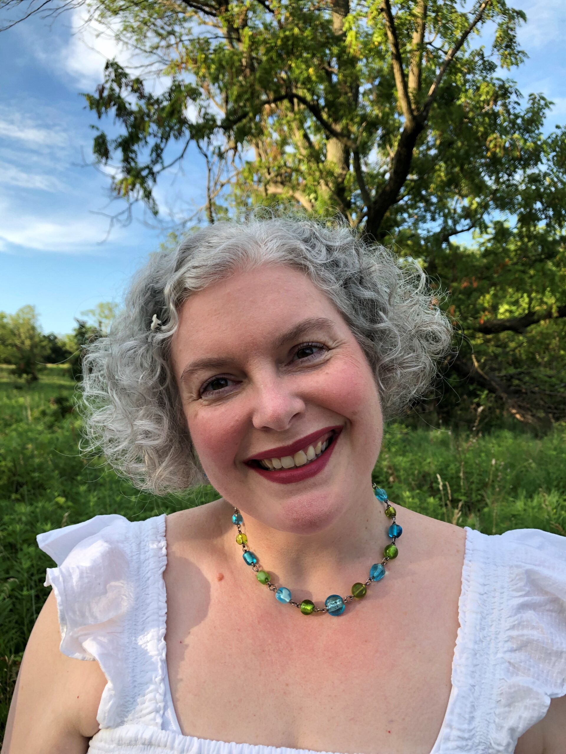 Cindy McKendall smiles at the camera while surrounded by nature and a blue sky