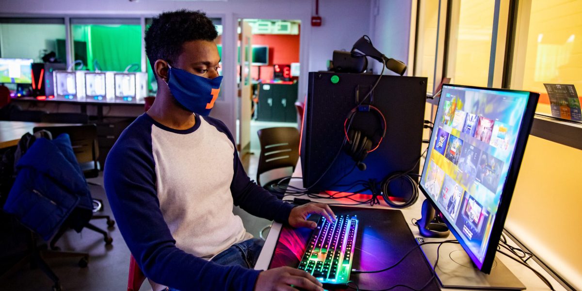 student wearing a mask issitting in chair using two computer monitors with mouse and keyboard